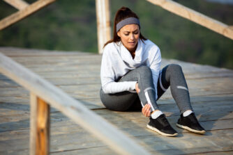 Young sportswoman experiencing pain in her leg while having sports training in nature.